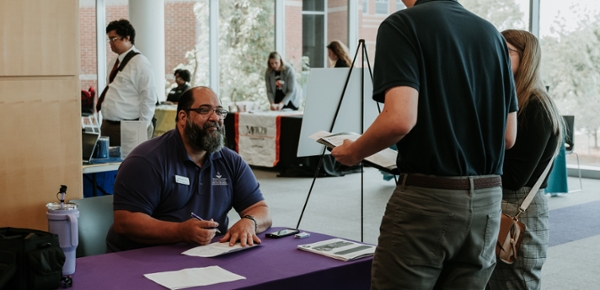 MGA worker speak with students at a career fair.